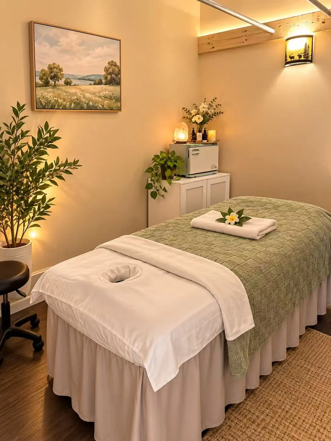 Massage table with a sage-green blanket and white face cradle under a landscape painting