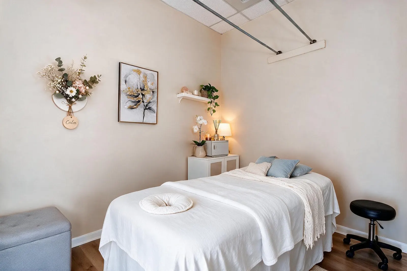 A massage table in white linens with blue pillows, a lamp and a small wall sign reading Calm